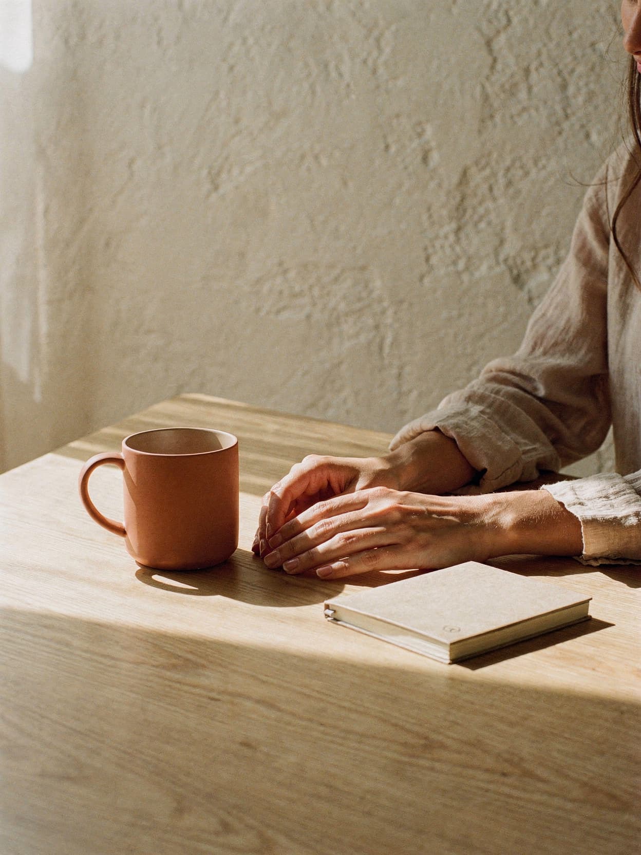 Marisol's hands resting on a kitchen table beside a mug and a notebook